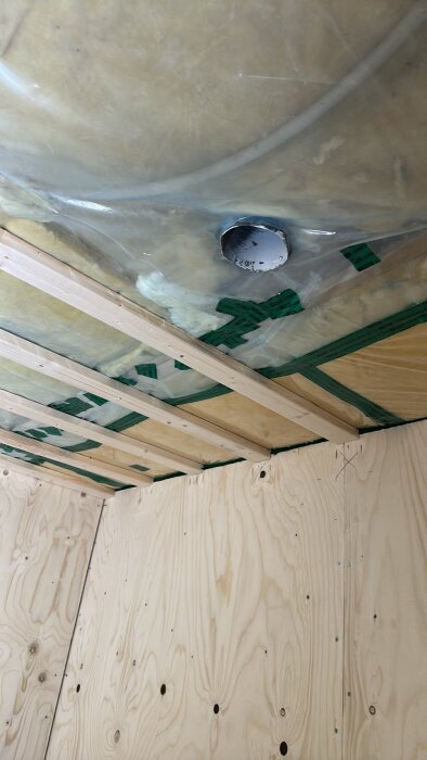 Tak- och väggkonstruktion med träreglar och plywood, isolering synlig under plastfolie, förberett för infällda spotlights.