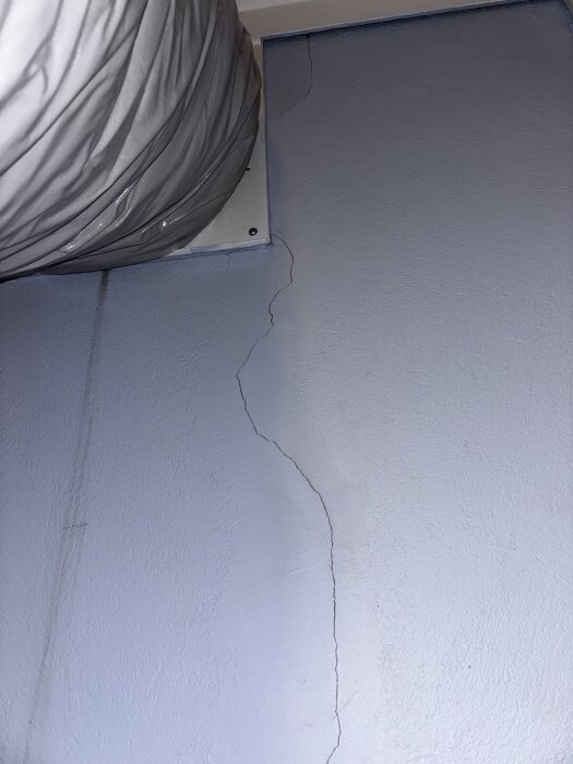 Spricka i källarvägg, cirka 1-2 mm bred, nära ett ventilationsrör, potentiellt orsakad av tidigare vattenläcka eller naturliga rörelser.