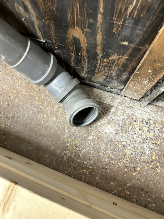 Avloppsrör synligt mot en mörk trävägg på byggarbetsplats, rörsystemets avslutning i fokus.