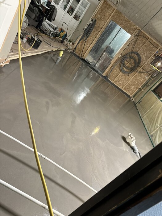 Nylagt flytspackelgolv i ett rum under renovering, med byggmaterial och utrustning runt omkring.
