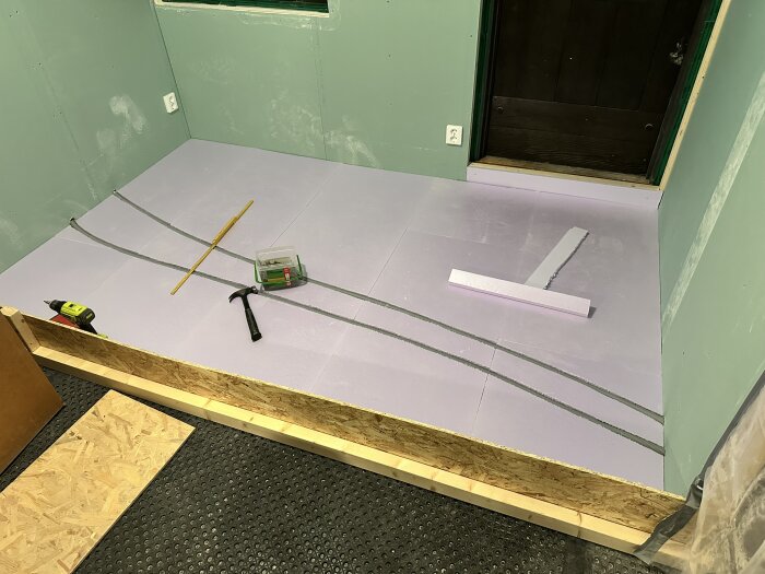 Golv under renovering med isoleringsskivor och verktyg som hammare och skruvdragare på plats, förberett för vidare byggarbete.
