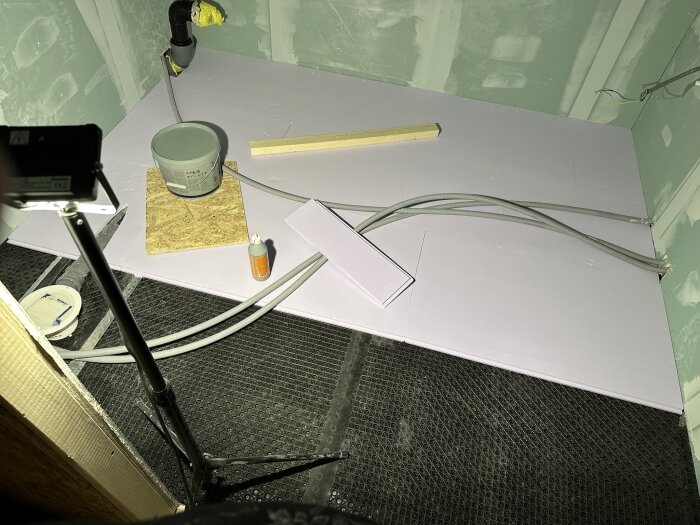 Renoveringsarbete i pågående stadie med isoleringsmaterial, rörinstallationer och verktyg i tomt rum med gipsskivor på väggarna.
