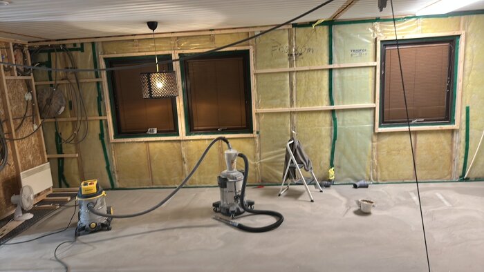 Renovering med flytspackling; rum med väggisolering, två fönster, dammsugare och stege. Golvet nyligen flytspacklat.