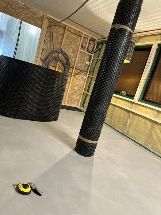 Rum med nylagt flytspackel, isolerad vägg och rullar av Jape Ventgolv. Verktyg syns på golvet, vilket förbereds för vidare renovering.