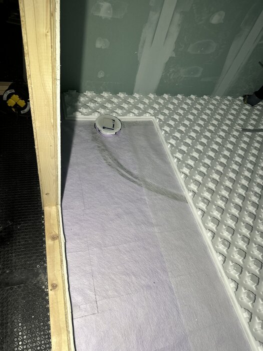 Golvarbete med isoleringsskiva och cellplast i fjällstruktur i badrum. Vit yta förberett för golvvärmeslangar med träreglar på sidan.