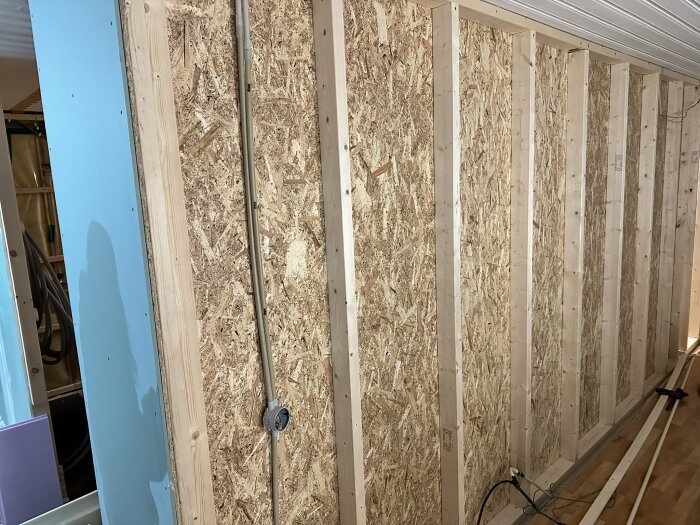 Väggkonstruktion av träreglar och OSB-skivor, delvis synlig elinstallation, under bygget av golvvärmesystem i rum under renovering.