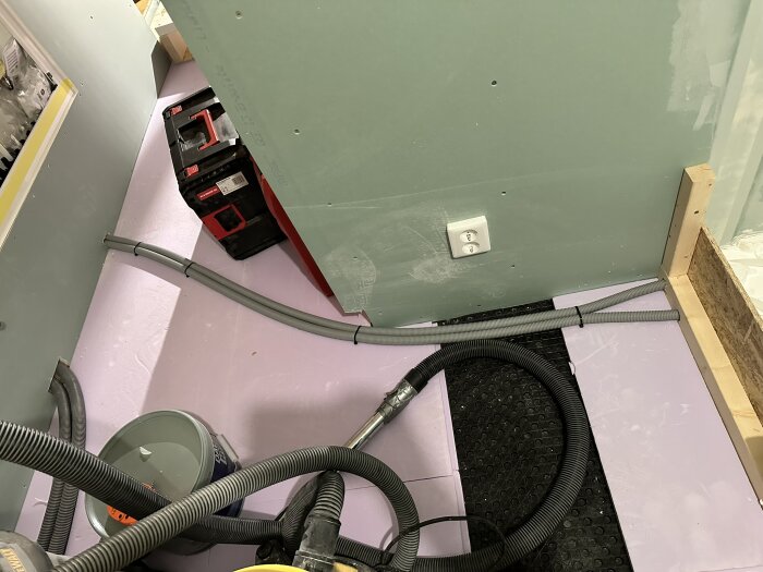Golvyta med golvskivor, rördragning och verktyg i en byggarbetsplats, där golvvärmesystem installeras och förbereds.