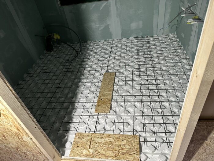 Golv med LK Systemskiva för golvvärmeslang i ett rum under renovering, gipsväggar, synliga rör och plastdetaljer. Plan för installation av golvvärme.