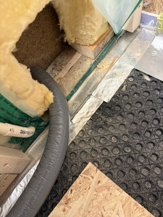 Isolering och rör i vägginstallation med cellplast, skivor och rör vid byggarbete i badrum eller hall.