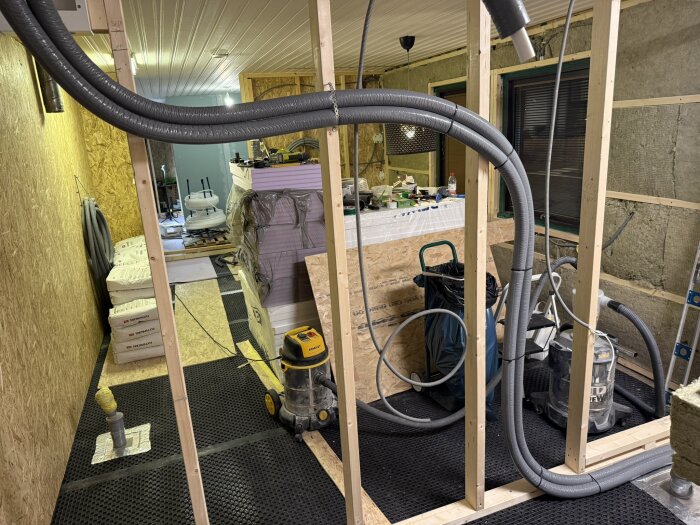 Renoveringsarbete med synlig golvvärmeslang i installationsfas. Byggmaterial och verktyg syns i bakgrunden i ett ofärdigt rum.