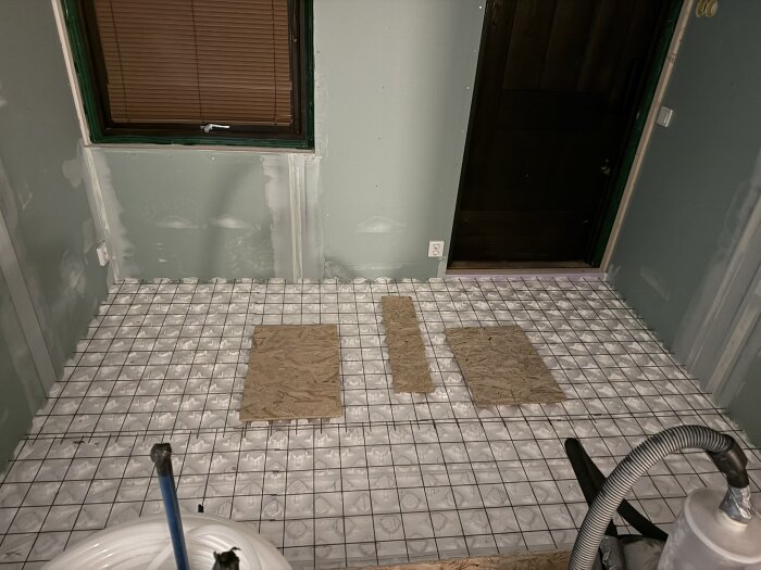 Under renovering, ett rum med golv bestående av armeringsnät. Två skivor placerade på golvet. Synlig slangrulle i förgrund.