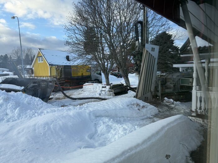 Borrigg vid gul byggnad i snötäckt landskap där arbete med borrning pågår, omgiven av träd och utrustning.