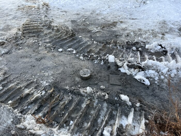 Mark med snötäckta traktorspår och ett runt betongfundament synligt på en vintertomt.