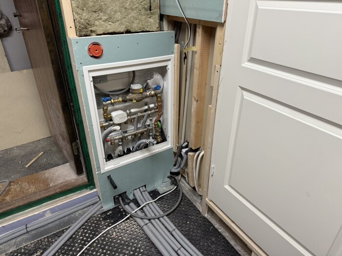 Golvvärmefördelare installerad i ett tekniskt utrymme med flera anslutna rör och kabeldragning genom väggen.