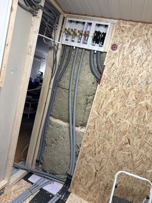 Installationsvägg med flera slangar och rör kopplade till en fördelningscentral i ett renoveringsprojekt med OSB-träpanel runtom.
