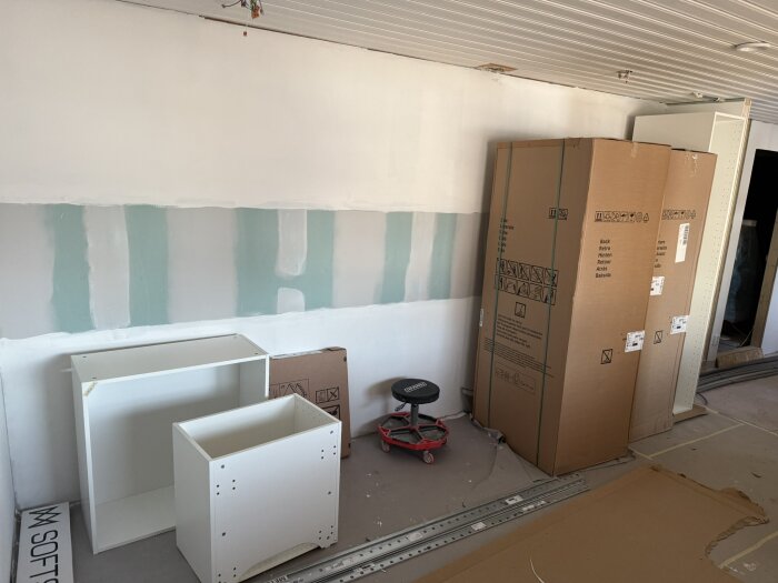 Köksrenovering med målade väggar, IKEA-skåp och stommar under montering, kartonger och en verktygsstol på golvet.