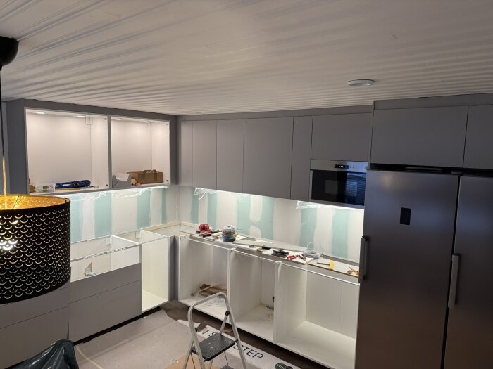 Nymonterat kök under renovering med grå skåp och vitvaror, ofärdiga väggar och förberedelser för bänkskiva, verktyg och material syns.