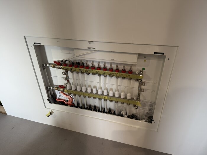 Golvvärmefördelare installerad i en väggmonterad skåp med rör och kopplingar synliga, redo för inkoppling i byggprojekt.