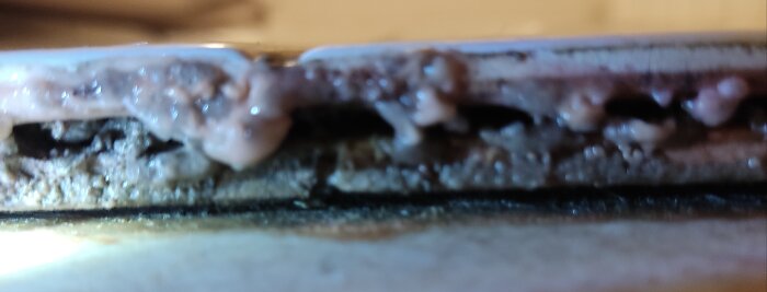 Närbild av vad som kan vara dubbla kakellager med misstänkt mögelväxt mellan lagren.