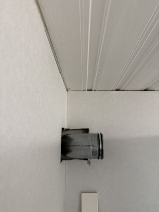 Ett grått ventilationsrör går genom en vit vägg nära taket, del av installation inom renovering.