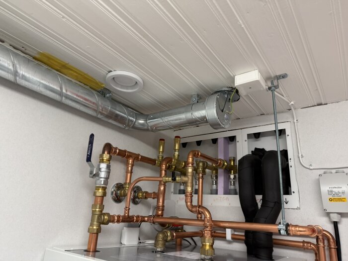 Ventilations- och rörinstallation med kopparrör och ventilationsrör i taket till en tvättstuga.