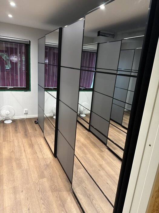 Spegelglasgarderober i ett rum med trägolv och fläktar, del av en renoveringsprocess i samband med IKEA PAX garderobsinstallation.