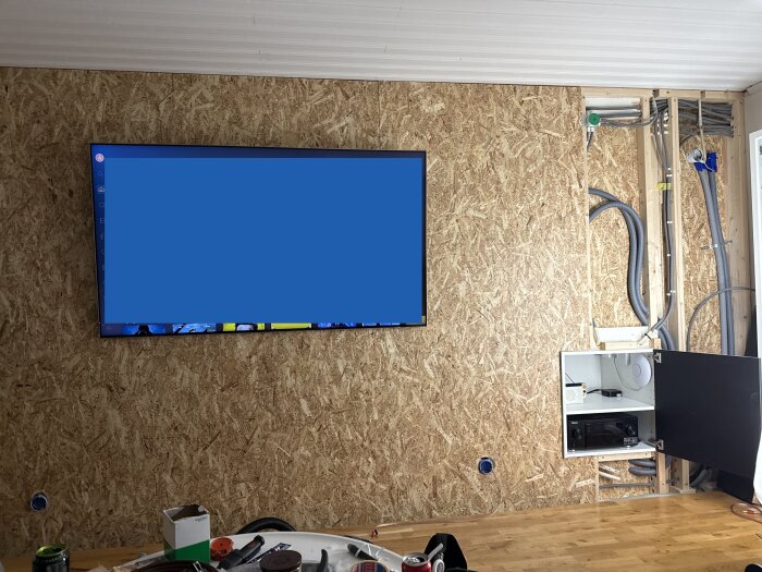 Vägg i träfiber med inbyggd TV och öppet skåp, synliga reglar och kablar förbereds för dold installation i ett renoveringsprojekt.