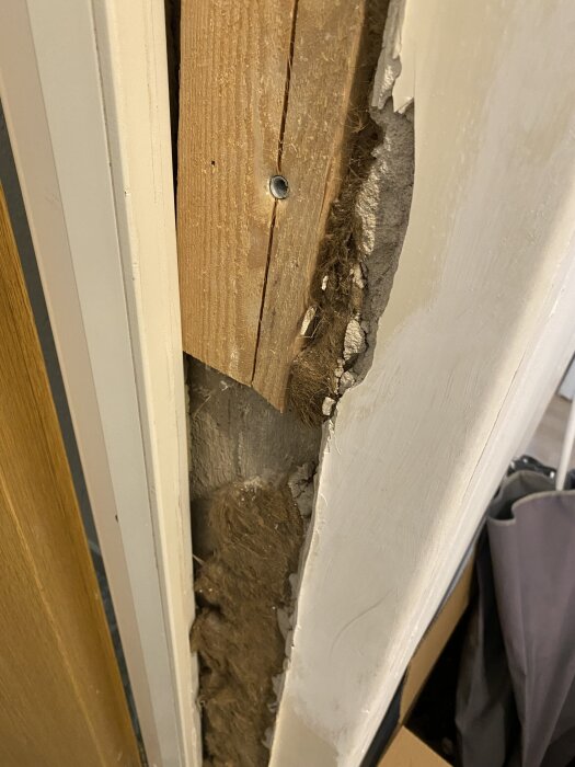 Skadad puts och trä i dörrkarm efter borttagning av plåtinklädnad, exponerar isolering, med fokus på renoveringsbehov.