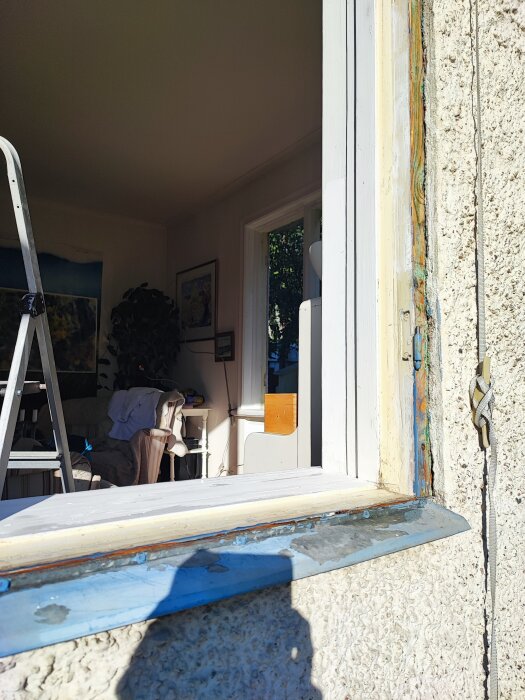 Fönsterrenovering i gammalt hus från 1923 med reveterad fasad, synliga sprickor i fogarna runt karmen, stege till vänster om fönstret från insidan.