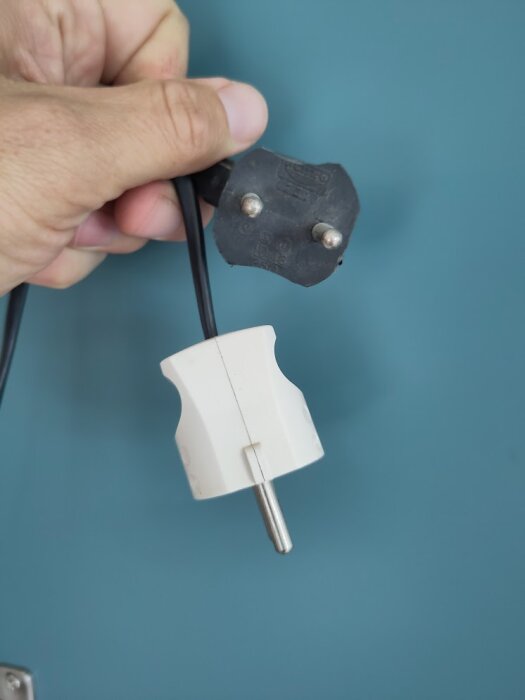 Hand håller ett svart och vitt eluttag och adapter mot blå bakgrund.