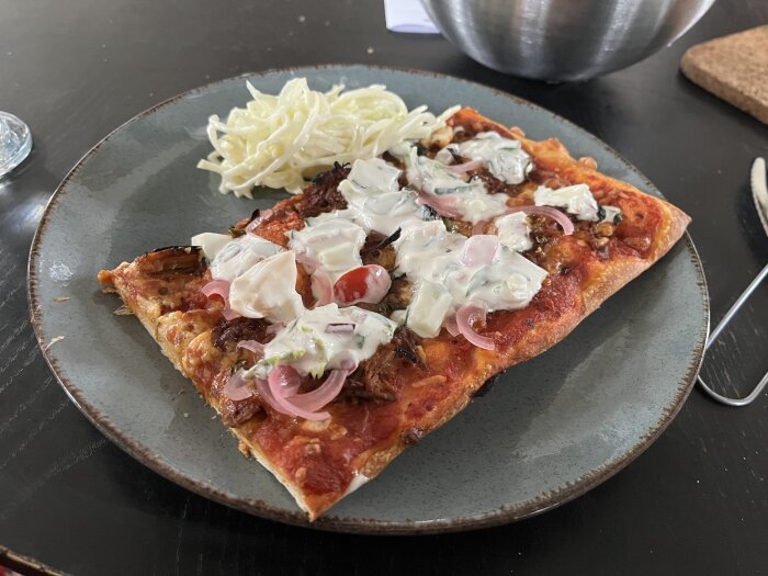 Hemgjord pizza med pulled pork, burrata, picklad rödlök och vitlökssås, serverad med coleslaw på en tallrik.