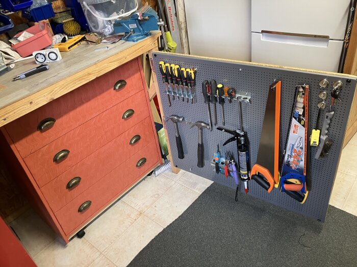 Röd arbetsbänk med lådor och en verktygspegboard på gångjärn, fylld med olika verktyg som hammare, skruvmejslar, såg och avbitartänger.