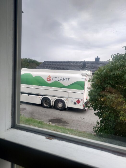 Tankbil från företaget Colabit parkerad utanför ett hus, sedd genom ett fönster.