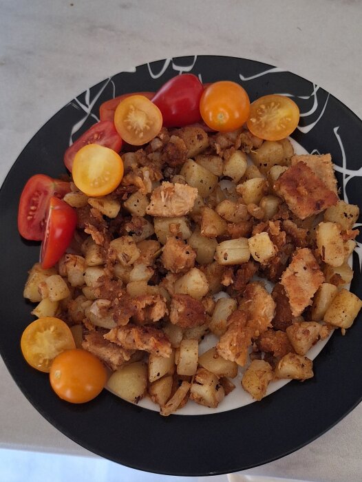 Pytt på vegoschnitzel, potatis och lök på svart tallrik, toppad med röda och gula tomater. Kryddad med salt, peppar och paprikapulver.