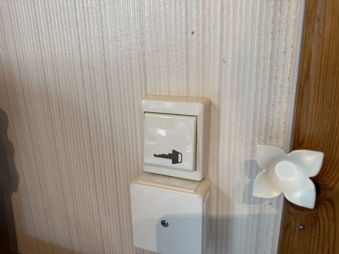 Väggmonterad fjädrande knapp med nyckelsymbol, installerad för att öppna dörren inifrån i ett smart hem projekt.