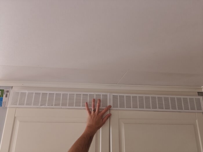 En hand justerar en ventilationsgaller ovanför en dörr.