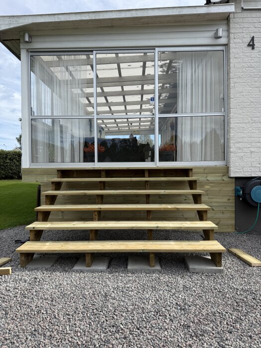 Trätrappa under uppbyggnad med bred design framför inglasad veranda, stommen klar och snart klädd med trallbrädor och förberedelse för decklights.