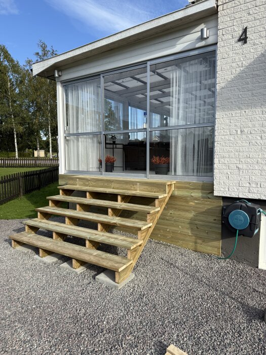 Bred trätrappa vid husfasad klar för nästa steg i byggprojekt. Stommen byggd, decklights och trallbrädor planeras för enhetligt utseende.