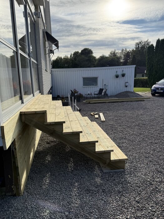 Bred entrétrappa av trä med färdig stomme vid husvägg, decklights och tralldetaljer ska tillkomma, grusgång runtom.