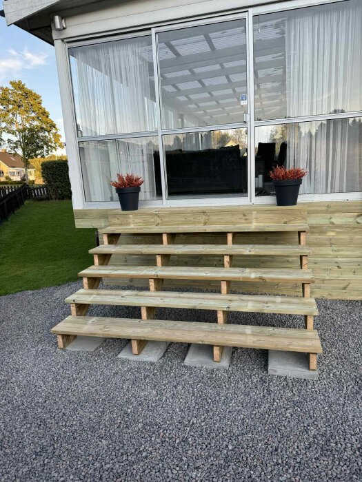 Bred trappa under konstruktion med trästomme och sex steg utanför ett inglasat uterum.