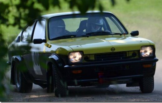 En gul och svart rallybil kör på en grusväg, fotad under en tävling. Bilen är en äldre modell ägd av någon annan vid fototillfället.