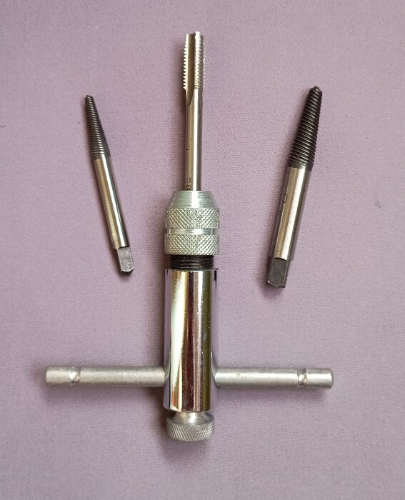 Hållare för gängtappar i metall, med tre skruvurdragare bredvid, som visas på lila bakgrund.