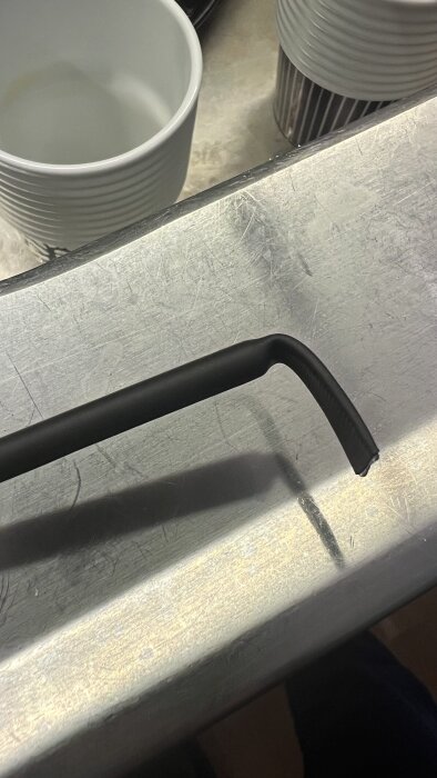 Svart krympslang med lim applicerad på en metallväxtstöd, fotograferad på en metallbänk.