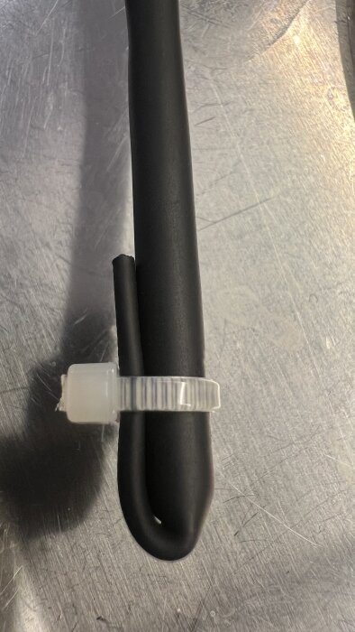 Svart krympslang med lim fäst runt ett växtstöd, säkrat med ett vitt plastbuntband.