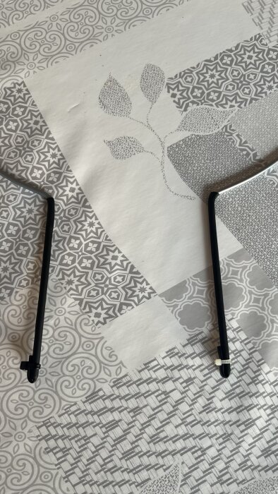 Två växtstöd täckta med krympslang och fästa med buntband på ett mönstrat underlag.