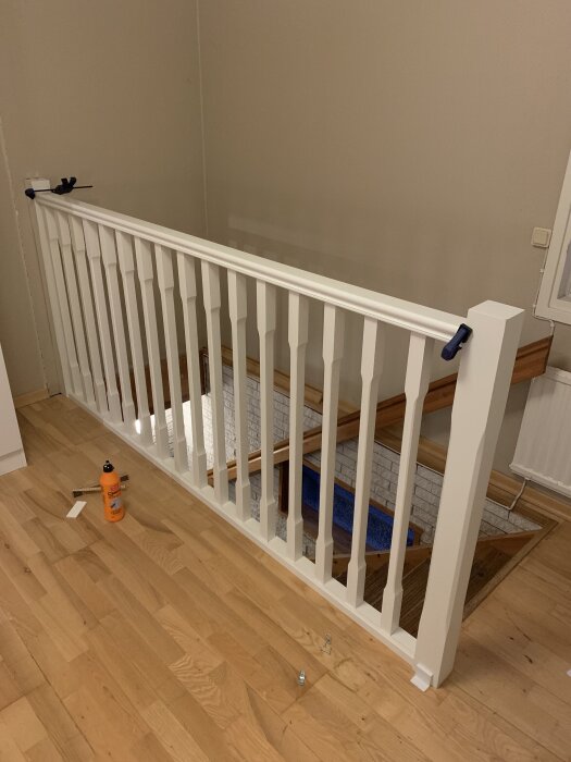 Nyinstallerat vitt trappräcke vid trappa, verktyg och lim syns på golvet.