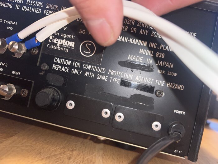 Närbild av baksidan på en elektronisk apparat med märken och varningar, inklusive Harman-Kardon Model 930, samt kablar och skruvar.