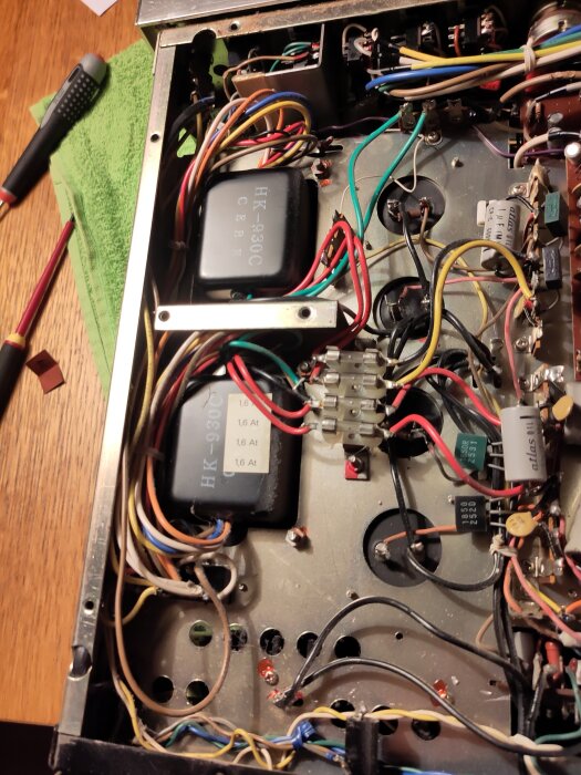 Elektroniskt kretskort med synliga kablar och komponenter, inklusive en transformator och säkringshållare. Verktyg ligger på bordet bredvid.