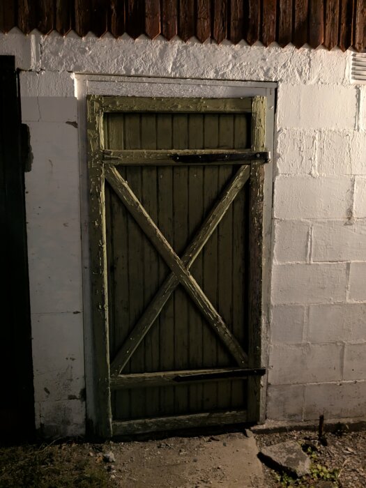 Sliten träport med diagonalt kors, omgiven av vitmålad betongvägg, eventuellt för renovering med leca-block.
