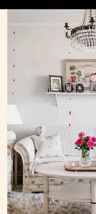 Vägg med sprickor markerade i rött, synliga till vänster om hylla med tavlor och under hyllan. Lampa, soffa och blommor i förgrunden.